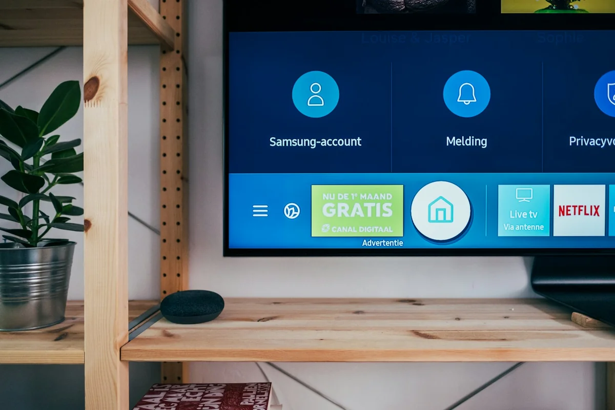 A smartphone in focus alongside a smart TV displaying streaming apps — illustrating the multi-platform comparison between IPTV One and TiviMate